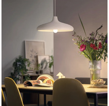 Moderne Pendelleuchte über einem Esszimmertisch mit Blumenstrauß und Dekoration im Hintergrund in einem hellen Wohnraum.