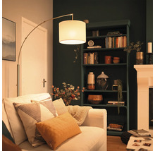 Moderne Bogenlampe mit Stoffschirm neben einem Sofa in einem gemütlich eingerichteten Wohnzimmer mit dunklem Regal und Kamin.