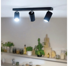 Deckenstrahler mit drei zylinderförmigen Lichtquellen an einer rechteckigen Leiste zur direkten Beleuchtung in einem Wohnbereich.