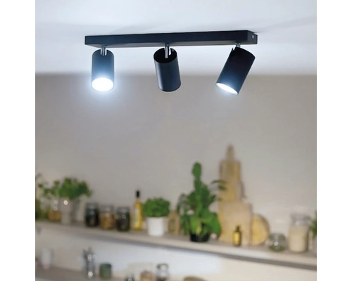Deckenstrahler mit drei zylinderförmigen Lichtquellen an einer rechteckigen Leiste zur direkten Beleuchtung in einem Wohnbereich.