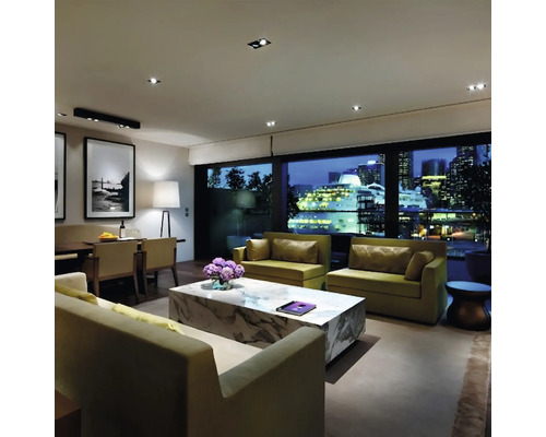 Modernes Wohnzimmer mit Sofas, Marmor Couchtisch und Blick auf ein Kreuzfahrtschiff in der nächtlichen Stadt bei moderner Innenbeleuchtung.