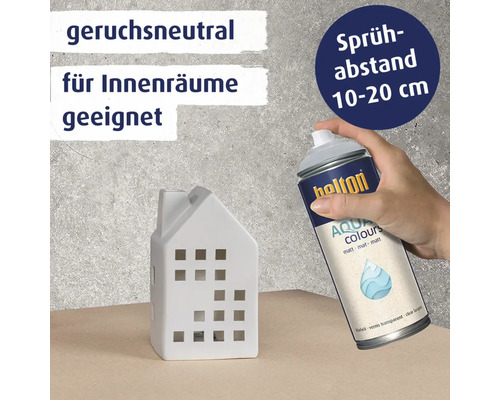Eine Hand sprüht mit einer Belton Aqua Colours Klarlack Sprühdose ein kleines Hausmodell ein mit dem Hinweis auf Sprühabstand und Innenraumnutzung.