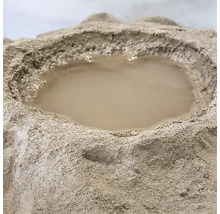 Ein Haufen aus trockenem Baustoffpulver mit einer Mulde in der Mitte, in der sich Wasser befindet, um den Mischvorgang vorzubereiten.