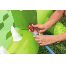 Hände beim Anschließen eines Gartenschlauchs an ein aufblasbares Wasserspielzeug auf einer Wiese.