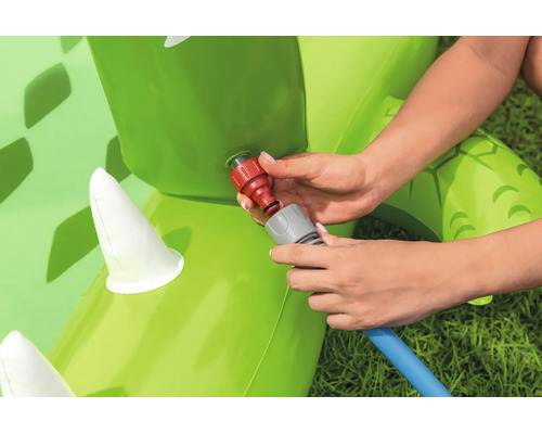 Hände beim Anschließen eines Gartenschlauchs an ein aufblasbares Wasserspielzeug auf einer Wiese.