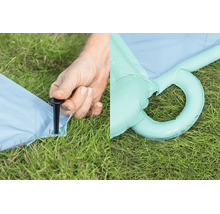 Person befestigt ein aufblasbares Produkt mit einem Bodenanker im Rasen, daneben ist eine aufblasbare Öse im Gras zu sehen.