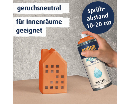 Eine Hand sprüht mit einer Belton Aqua Colours Sprühdose auf ein kleines Dekohaus. Die Farbe ist geruchsneutral und für Innenräume geeignet.