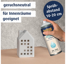 Eine Hand sprüht mit Helton Aqua Colours Lack in lichtgrau RAL 7035 auf ein weißes Deko Haus. Produktinformationen für Innenräume.