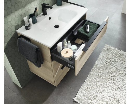Waschtischunterschrank in Holzoptik mit weißem Waschbecken und ausgezogener Schublade inklusive Ordnungssystem und Handtuchhalter im Badezimmer.