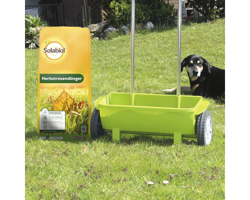 Solabiol Herbstrasendünger 10 Kilogramm Sack neben einem Streuwagen auf einer Wiese mit Hund im Hintergrund.