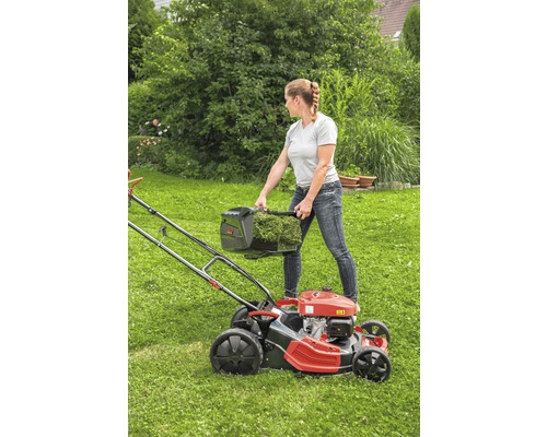 Eine Frau leert den Grasfangkorb eines Rasenmähers auf einer Rasenfläche.