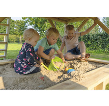 Drei Kinder spielen in einem Sandkasten aus Holz mit Spielzeug.