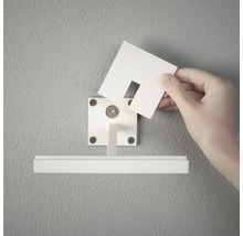 Person befestigt einen Sichtschutz an einer Gardinenstange an der Wand.