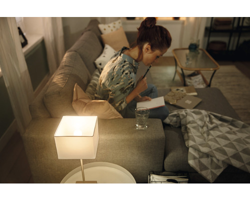 Frau sitzt auf einem Sofa und schreibt Notizen neben einer Tischlampe in einem Wohnzimmer.