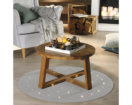 Wohnzimmer mit Sessel, Kamin und rundem Couchtisch auf einem Teppich mit Lichtpunkten