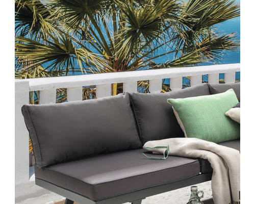 Nahaufnahme einer Loungegruppe mit Kissen, Decke und Palme im Hintergrund