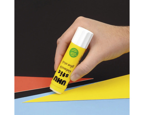 Eine Hand hält einen UHU Klebestift über farbigem Papier.
