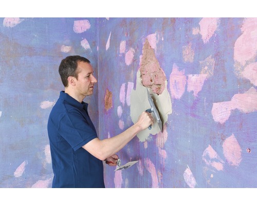 Ein Mann spachtelt ein Loch in der Wand mit einem Spachtel.