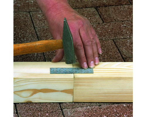 Handwerker befestigt eine Lochplatte mit einem Hammer an zwei Holzbalken