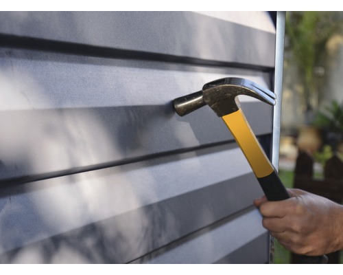 Ein Hammer wird verwendet, um einen Nagel in eine Holzverkleidung zu schlagen.