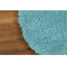 Detailansicht eines runden, hellblauen Teppichs mit hochflorigem Flor auf einem Holzboden.