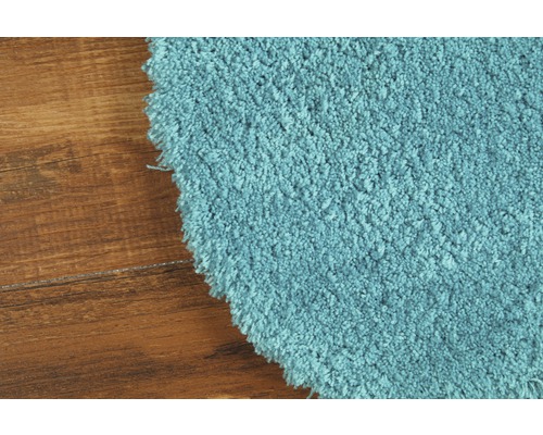 Detailansicht eines runden, hellblauen Teppichs mit hochflorigem Flor auf einem Holzboden.