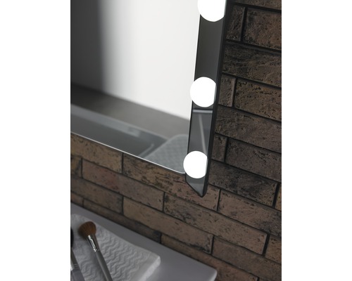 Detailansicht eines beleuchteten Spiegels neben einer Backsteinwand im Badezimmer