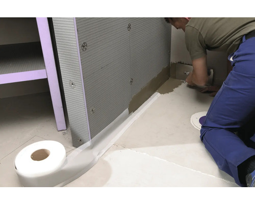 Badezimmerszene mit Abdichtband, Dämmplatten und Handwerker bei der Arbeit