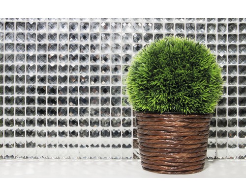 Dekorative grüne Kunstpflanze im braunen Topf vor einer Mosaikwand