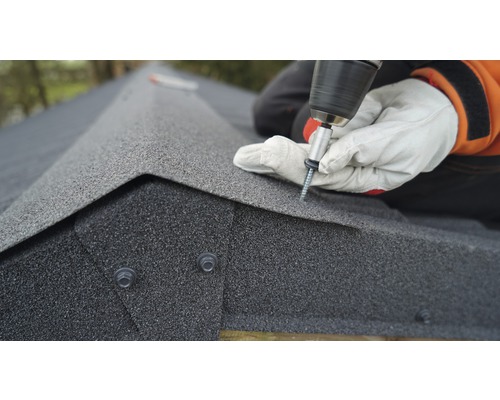 Ein Handwerker befestigt Dachschindeln mit einem Akkuschrauber auf einem Dach.