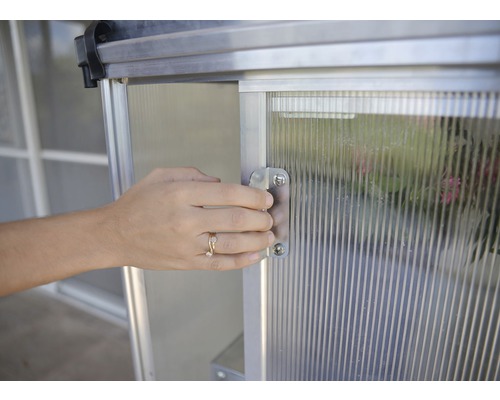 Eine Person öffnet die Tür eines Gewächshauses.