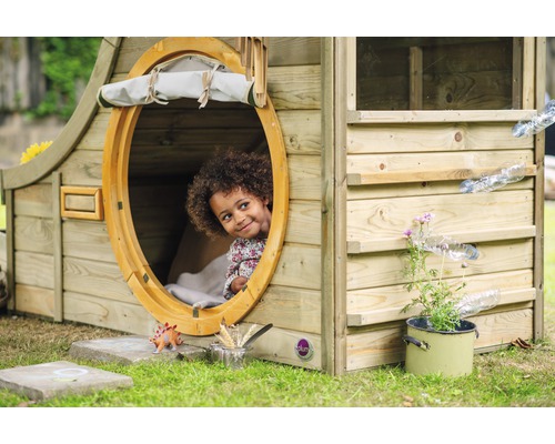 Ein Kind schaut aus einem runden Fenster eines Holzspielhauses mit Wasserspiel.