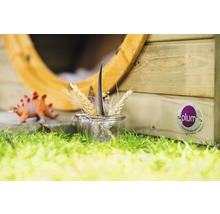 Szene mit Spielhaus, Dinosaurier Spielzeug und einem Glas mit Weizenähren und einer Feder auf einer Rasenfläche. Plum Logo sichtbar.
