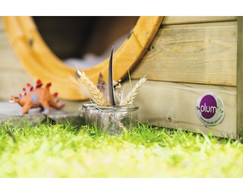 Szene mit Spielhaus, Dinosaurier Spielzeug und einem Glas mit Weizenähren und einer Feder auf einer Rasenfläche. Plum Logo sichtbar.