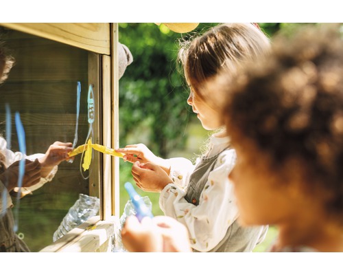 Zwei Kinder malen mit Stiften auf eine Glasscheibe in einem Spielhaus