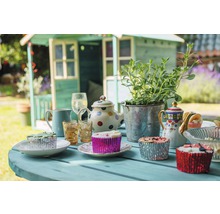 Gedeckter Tisch mit Gartenhaus im Hintergrund für eine Gartenparty mit Teekannen, Pflanzen, Gläsern und Muffins.