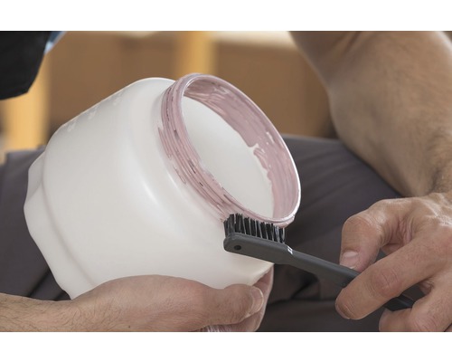 Eine Person reinigt einen Farbeimer mit einer Bürste.