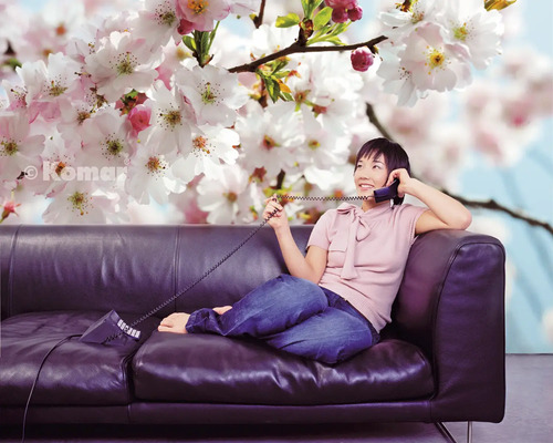 Frau telefoniert vor einer Fototapete mit Kirschblüten auf einem Sofa