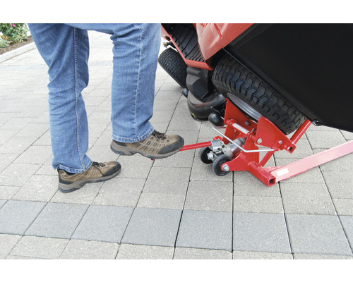 Eine Person betätigt einen Rasentraktorheber mit dem Fuß.