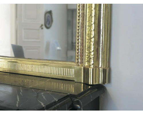 Detailaufnahme eines Spiegels mit goldenem Rahmen auf einem schwarzen Marmorsims