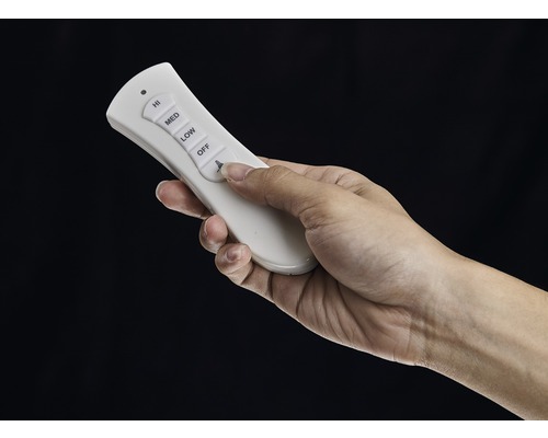 Eine Hand bedient eine weiße Fernbedienung für einen Deckenventilator.
