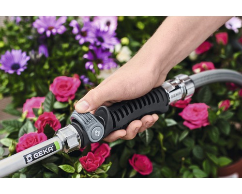 Eine Hand hält einen Gartenschlauch mit GEKA-Kupplung vor einem Blumenbeet.