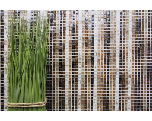 Dekorative grüne Kunstpflanze vor einer Mosaikwand aus Glas