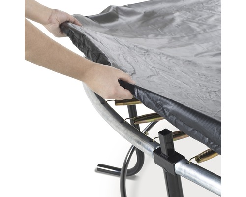 Person legt eine Trampolin Schutzplane über ein Trampolin