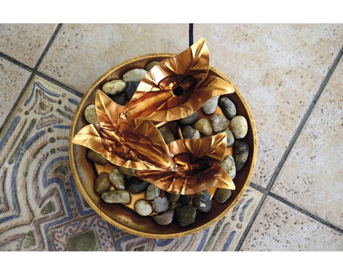 Dekorativer Zimmerbrunnen mit goldenen Blättern und Kieselsteinen in einer Schale