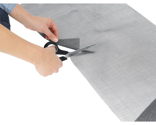 Eine Person schneidet ein Insektenschutzgitter mit einer Schere.