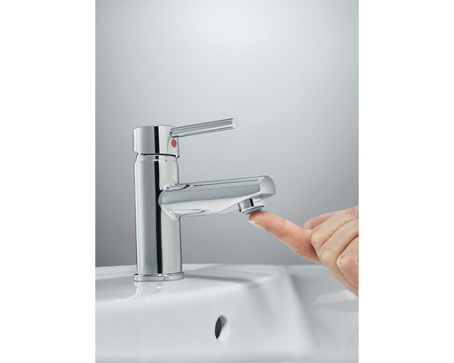 Glänzender Wasserhahn mit Finger auf dem Auslauf in einem Waschbecken