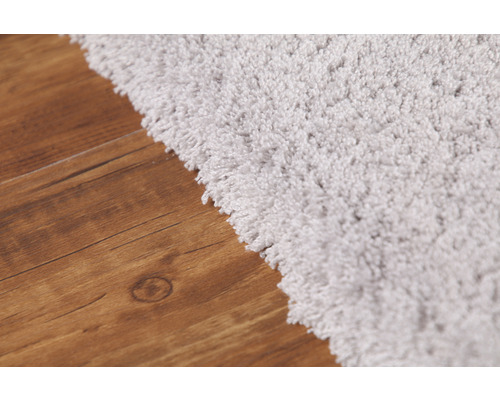 Detailansicht eines hellen Hochflor Teppichs auf einem Holzboden