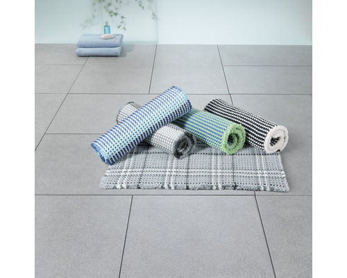 Mehrere Badezimmerteppiche in verschiedenen Designs gerollt und gestapelt im Badezimmer.