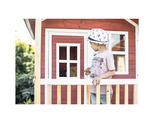 Kind vor einem Spielhaus aus Holz mit Fenster und Zaun